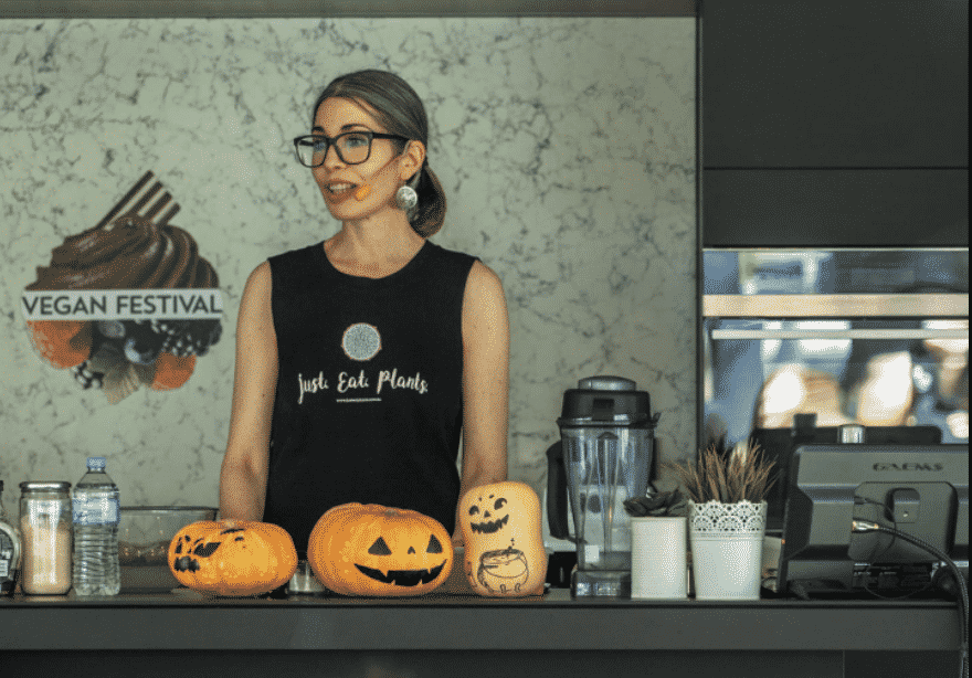 A women with a short ponytail providing a cooking demonstration with pumpkins and a blender 